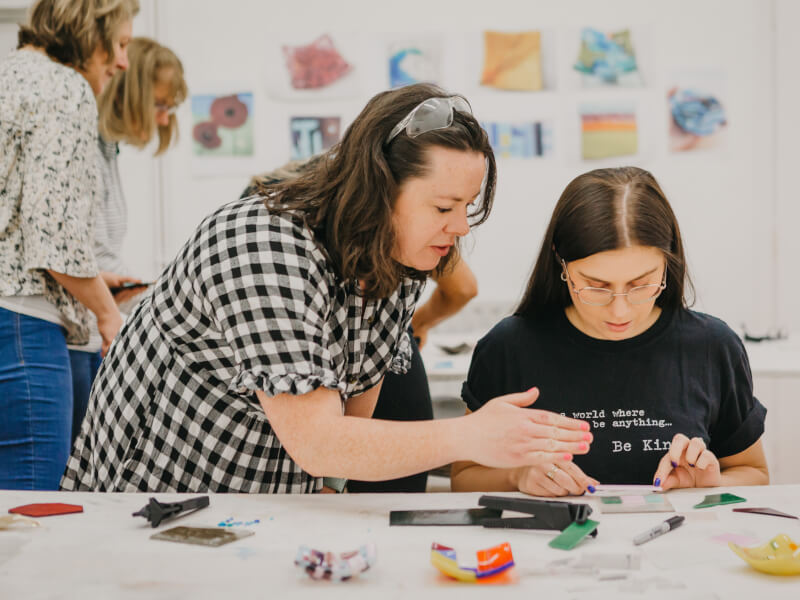 A woman guides a student in a glass fusing class.